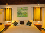 Desert Villa Boutique Hotel room with double bed, white linens, green patterned cushions, wooden nightstands, yellow curtains, and green artwork