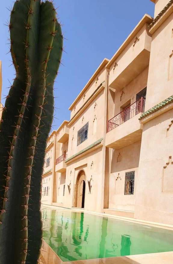 Desert Villa Boutique Hotel exterior in sandy beige with green-tiled roof and reflective pool beside tall cactus plant