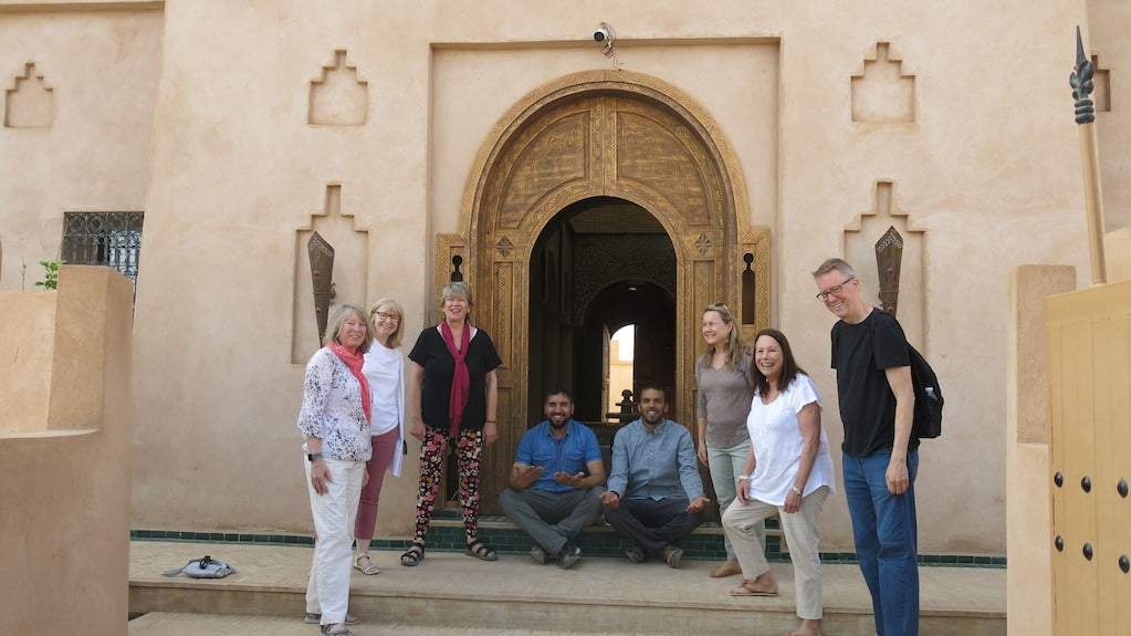 Desert Villa Boutique Hotel group of seven people posing in front of a large ornate wooden arched doorway with beige stucco walls