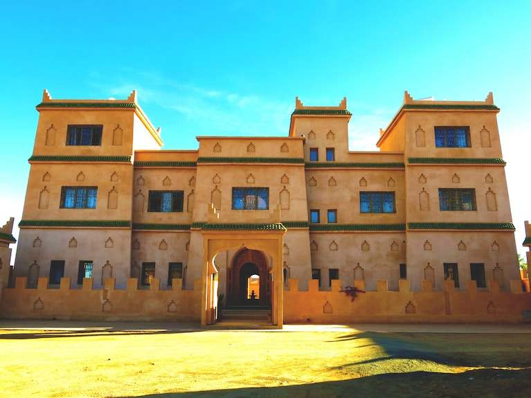 Desert Villa Boutique Hotel in beige stucco with traditional Moroccan architectural details and green tile accents under a clear blue sky