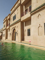 Desert Villa Boutique Hotel with beige stucco walls, Moroccan-style windows, and a green-tiled roof beside a turquoise swimming pool