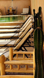 Desert Villa Boutique Hotel outdoor pool area with cream lounge chairs and wooden furniture beside tall cacti plants under beige walls