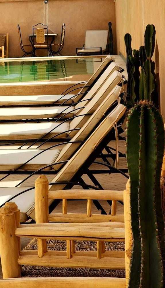 Desert Villa Boutique Hotel outdoor pool area with cream lounge chairs and wooden furniture beside tall cacti plants under beige walls
