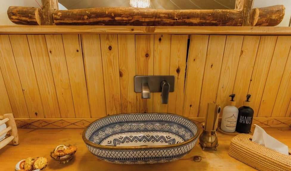 Decorative ceramic washbasin with intricate blue patterns set on a wooden countertop in Dihya Desert Camp bathroom