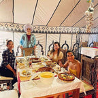 Dihya Desert Camp dining tent with four people enjoying traditional Moroccan dishes on a decorated table with patterned fabric walls