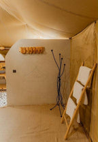 Dihya Desert Camp interior with beige tent fabric, smooth plastered wall, wooden towel rack, and black metal coat stand