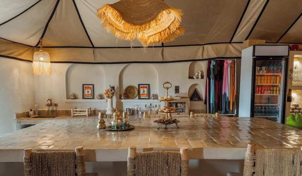 Dihya Desert Camp interior with beige tiled counter, wicker chairs, rustic decor, and hanging woven lampshades