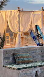 Dihya Desert Camp outdoor seating with flowing white curtains, wooden chairs, and patterned cushions on stone benches in desert
