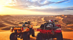Two all-terrain vehicles, one orange and one red, parked on sandy dunes under a cloudy sky at Dihya Desert Camp