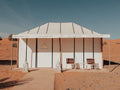 Dihya Desert Camp white canvas tent with tan trim set on sandy desert ground, featuring two wooden chairs and decorative lanterns