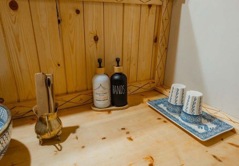 Dihya Desert Camp wooden bathroom counter with blue and white ceramic cups, branded soap and hand lotion dispensers, and a toothbrush holder