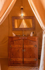 Wooden cabinet with metal hinges and a decorative framed mirror above, inside a beige tent at Dihya Desert Camp