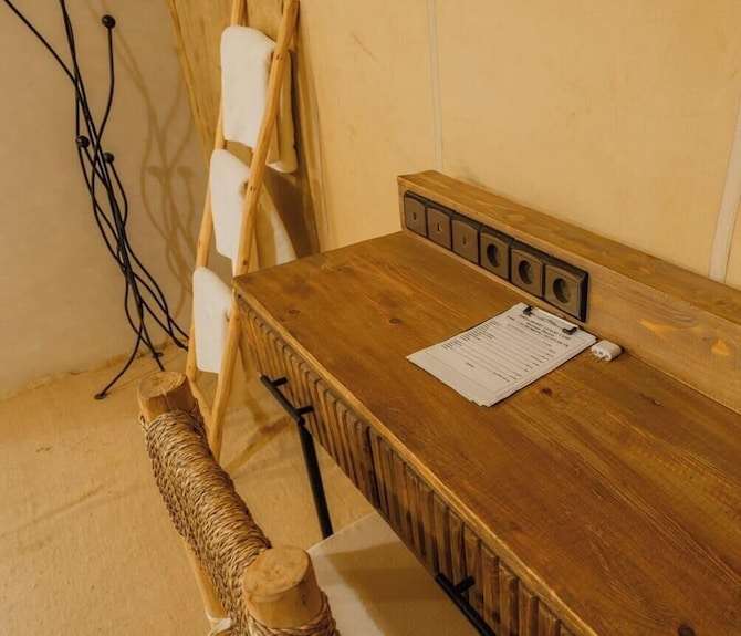 Dihya Desert Camp wooden desk with built-in power sockets and rustic woven chair in warm beige interior