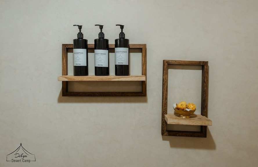 Dihya Desert Camp wall-mounted wooden shelves holding black dispenser bottles for shampoo, body wash, conditioner, and a decorative bowl with sponges