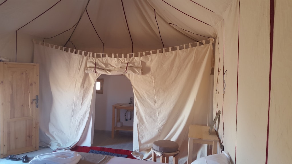 Erg Chigaga Star Camp beige canvas tent interior with wooden door, small stool, and light wooden furniture