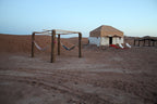 Erg Chigaga Star Camp with beige canvas tent, hammocks hanging on wooden posts, and sandy desert surroundings at dusk