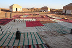 Erg Chigaga Star Camp outdoor area with colorful striped and patterned rugs spread on sandy ground surrounded by beige desert tents