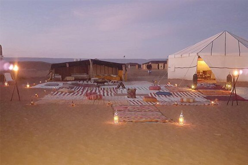 Erg Chigaga Star Camp with illuminated tent and traditional Moroccan rugs and cushions arranged on sandy ground at dusk