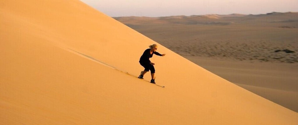 Person sandboarding down a large golden sand dune in the Erg Chigaga desert at Erg Chigaga Star Camp