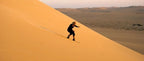 Person sandboarding down a large golden sand dune in the Erg Chigaga desert at Erg Chigaga Star Camp