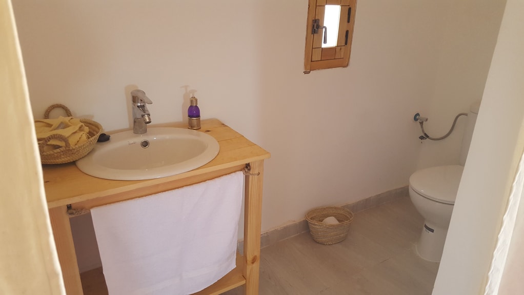 Erg Chigaga Star Camp simple bathroom with wooden sink countertop, white basin, small window, and white toilet