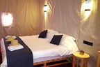 Erg Chigaga Star Camp tent bedroom with white bedding, dark blue pillows, natural wood furniture, and warm lighting