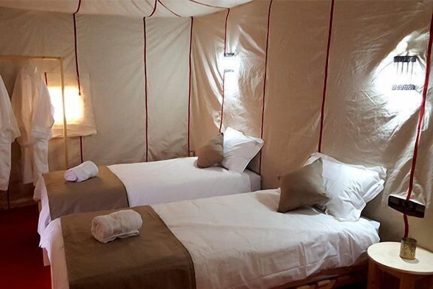 Erg Chigaga Star Camp interior with two single beds featuring white linens and brown runners inside a beige tent with red seams