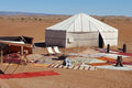Erg Chigaga Star Camp with a large white canvas tent surrounded by colorful rugs and chairs on desert sand