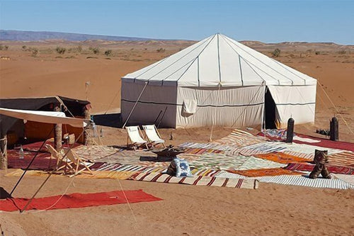 Erg Chigaga Star Camp with a large white canvas tent surrounded by colorful rugs and chairs on desert sand