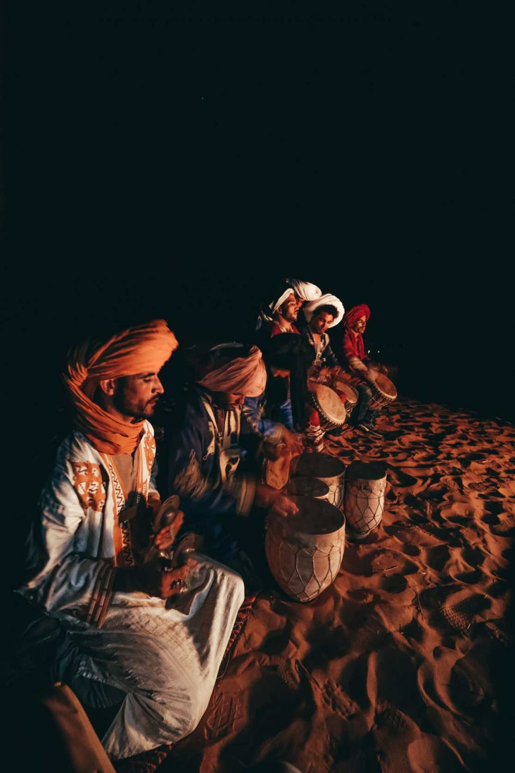 Errachidia Airport desert musicians wearing traditional Moroccan clothing playing drums on sand at night under dark sky