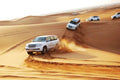 White 4x4 SUVs driving off-road through golden sand dunes under a clear sky, showcasing desert adventure near Errachidia Airport.