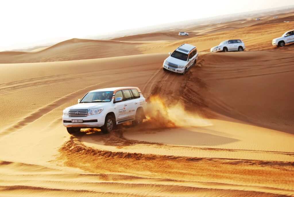 White 4x4 SUVs driving off-road through golden sand dunes under a clear sky, showcasing desert adventure near Errachidia Airport.