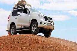White 4x4 vehicle equipped with roof luggage rack parked on sandy hill under blue sky showcasing adventure travel