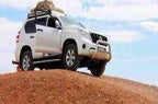 White 4x4 vehicle equipped with roof luggage rack parked on sandy hill under blue sky showcasing adventure travel