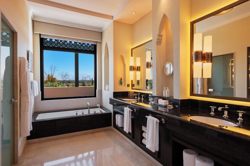 Four Seasons Resort Marrakech bathroom with black marble countertops, twin sinks, arched mirrors, large window, and soaking tub