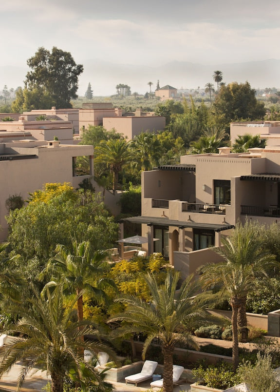 Four Seasons Resort Marrakech with beige stucco buildings, lush green palm trees, and landscaped gardens under a cloudy sky