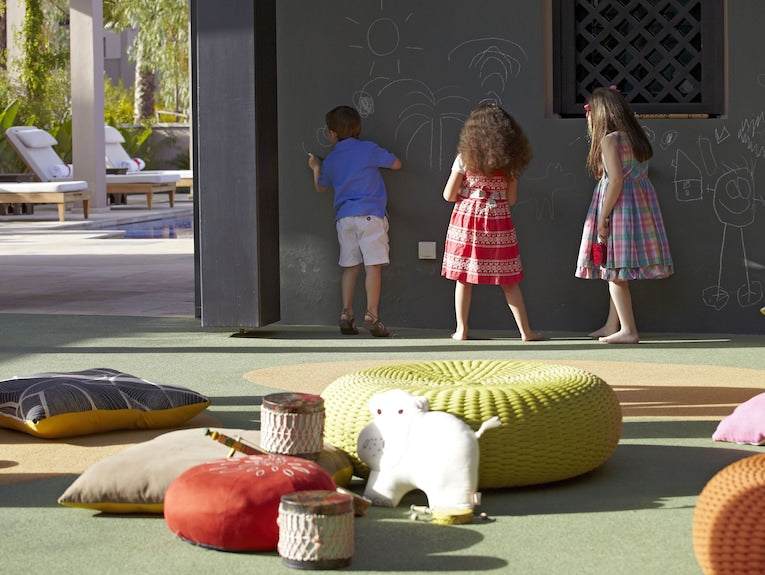 Children drawing on a black outdoor chalkboard wall at Four Seasons Resort Marrakech with colorful cushions and toys on green ground