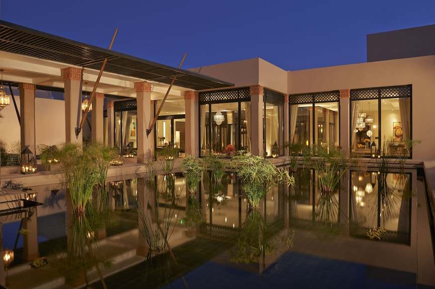 Four Seasons Resort Marrakech exterior view at dusk featuring Moroccan-inspired architecture with columns and reflective water garden
