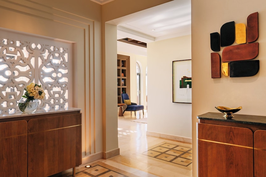 Four Seasons Resort Marrakech interior featuring warm beige walls, wooden cabinets, decorative lattice panel, modern art, and polished stone flooring
