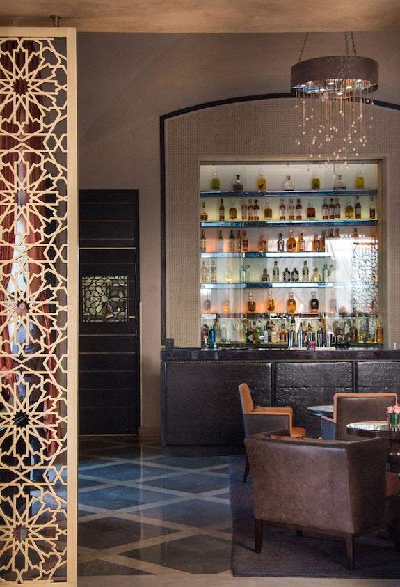 Luxury bar interior at Four Seasons Resort Marrakech featuring Moroccan patterned screens, dark wood chairs, and illuminated liquor shelves
