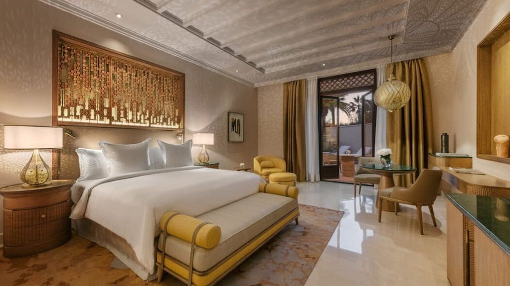 Four Seasons Resort Marrakech luxury bedroom with large white bed, yellow armchair, ornate wall decor, and balcony access