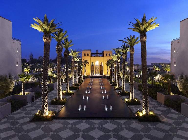 Four Seasons Resort Marrakech luxury hotel at dusk with illuminated palm trees, water fountains, and Moroccan-inspired architecture