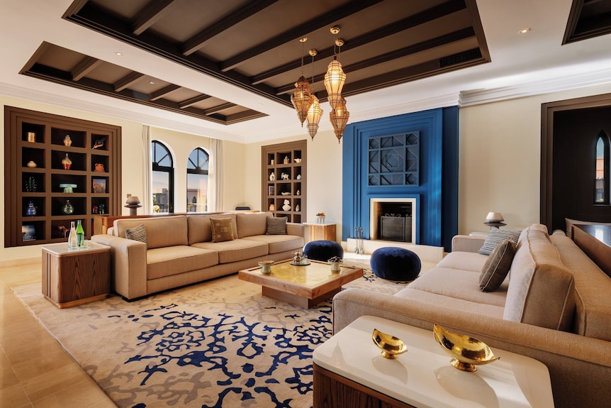 Luxury living room with beige sectional sofas, blue and beige patterned rug, blue fireplace, and Moroccan lanterns at Four Seasons Resort Marrakech