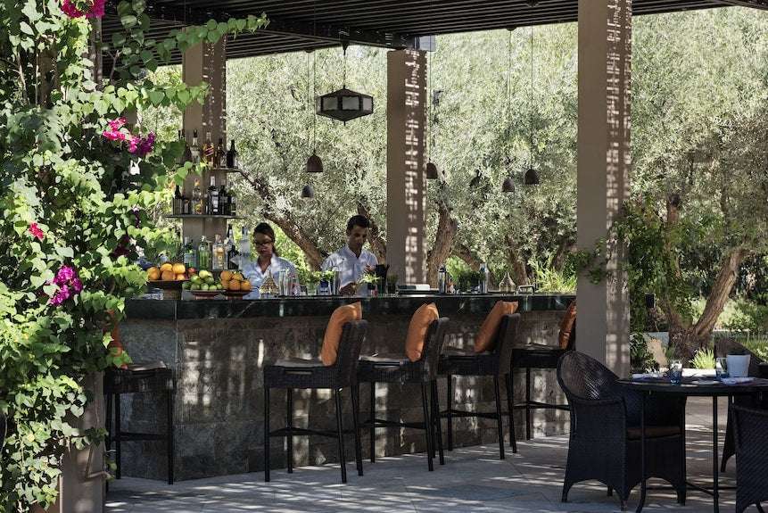 Four Seasons Resort Marrakech outdoor bar area with stone countertop, black chairs, green plants, and shaded patio