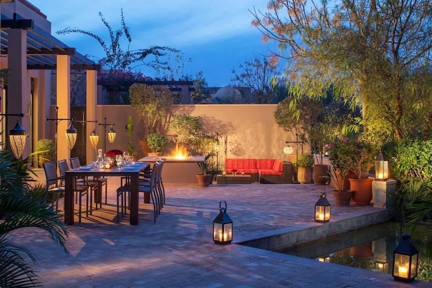 Outdoor patio area at Four Seasons Resort Marrakech with a dining table set for dinner, glowing lanterns, fire pit, and lush greenery at dusk