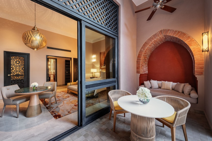 Outdoor patio seating area with white round table, wicker chairs, beige cushions, and Moroccan-style arch at Four Seasons Resort Marrakech