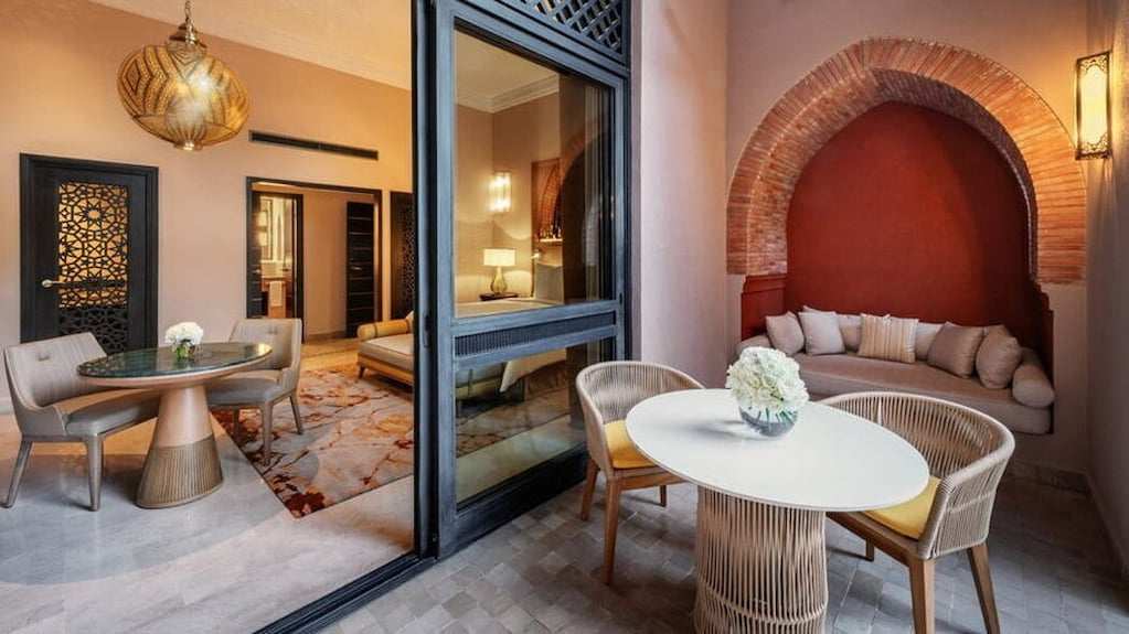 Four Seasons Resort Marrakech outdoor seating area with beige woven chairs, round and oval tables, and decorative brick arch