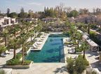 Four Seasons Resort Marrakech outdoor pool area with turquoise water, beige stone deck, palm trees, and sun loungers