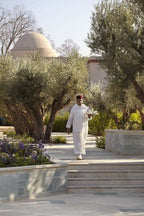 Four Seasons Resort Marrakech with a server in traditional white attire and red hat carrying a tray in a landscaped garden with olive trees and dome architecture