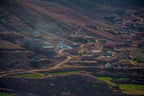 From Marrakech to Ourika Valley tour showing a rugged Atlas Mountain village with earthen homes, winding roads, and green fields